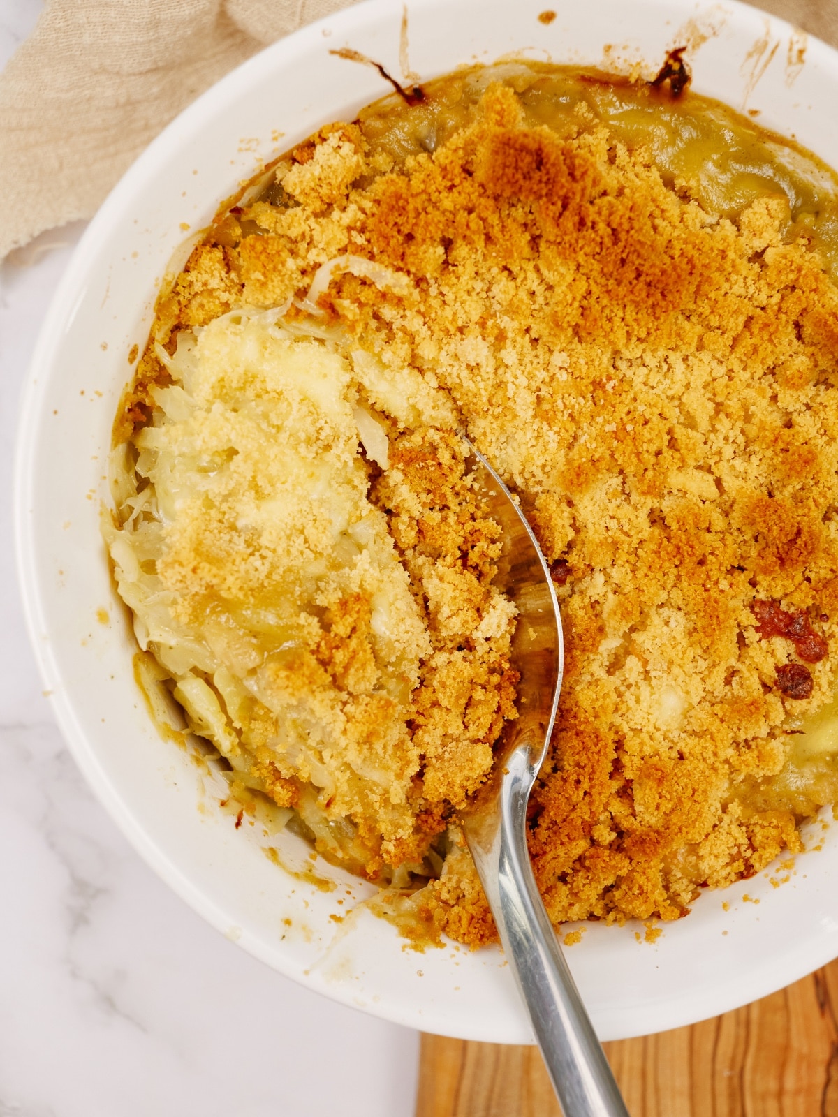 cabbage casserole baked in a round baking dish on a white marble surface with a spoon in the middle