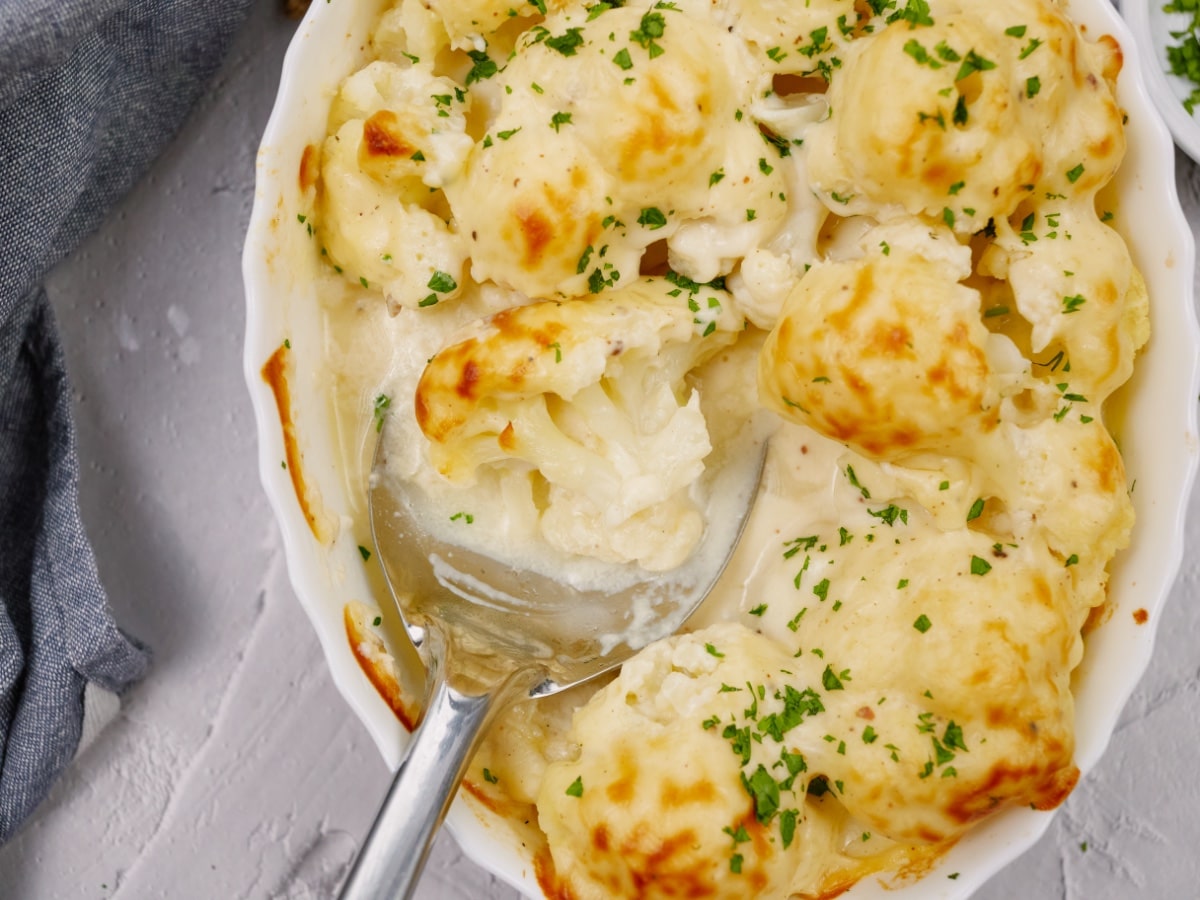 baked cauliflower casserole topped with minced chives in a white baking dish with a spoon in the middle