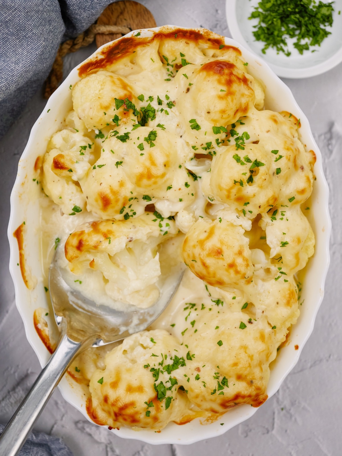 baked cauliflower casserole topped with minced chives in a white baking dish with a spoon in the middle