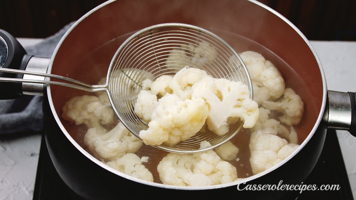 spooning out cooked cauliflower from a pot of water with a spider