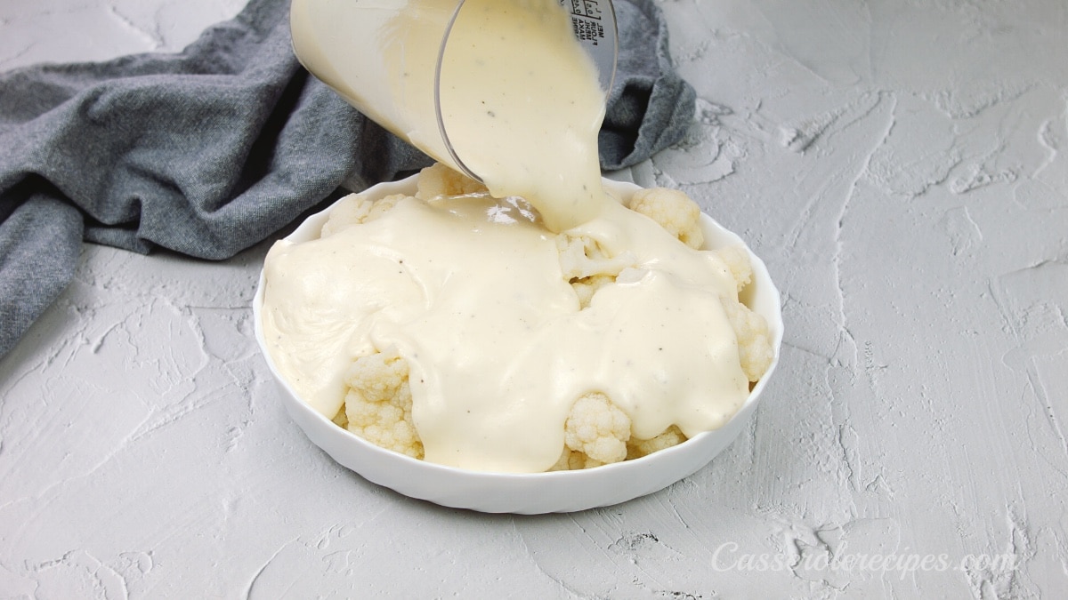 pouring sauce over cauliflower in a baking dish