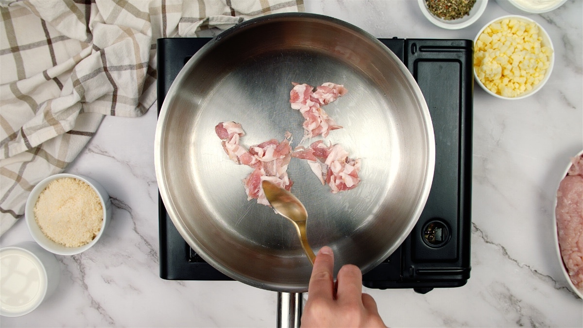 raw bacon in a saute pan being mixed with a fork