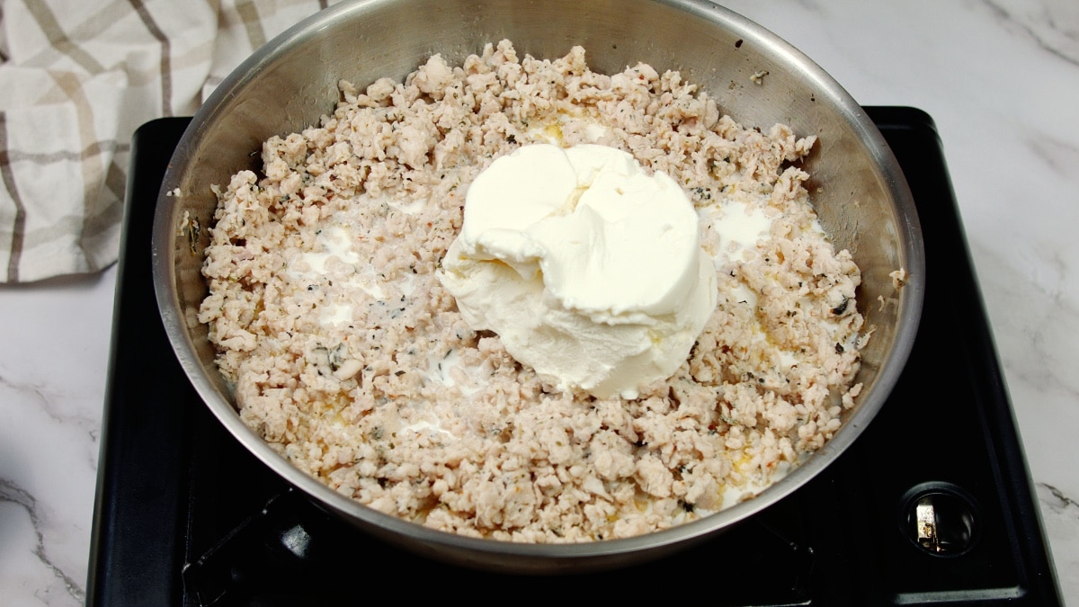 cooked ground chicken in a pan being topped with cream cheese