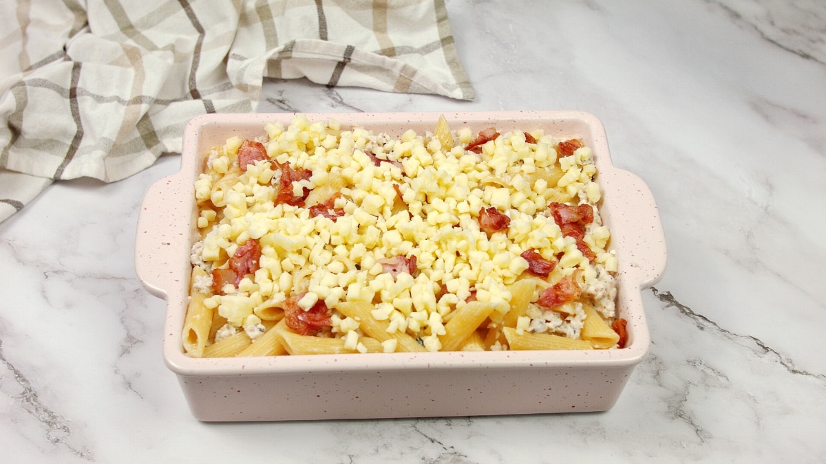 a casserole dish filled with chicken and pasta mixture and topped with shredded cheese