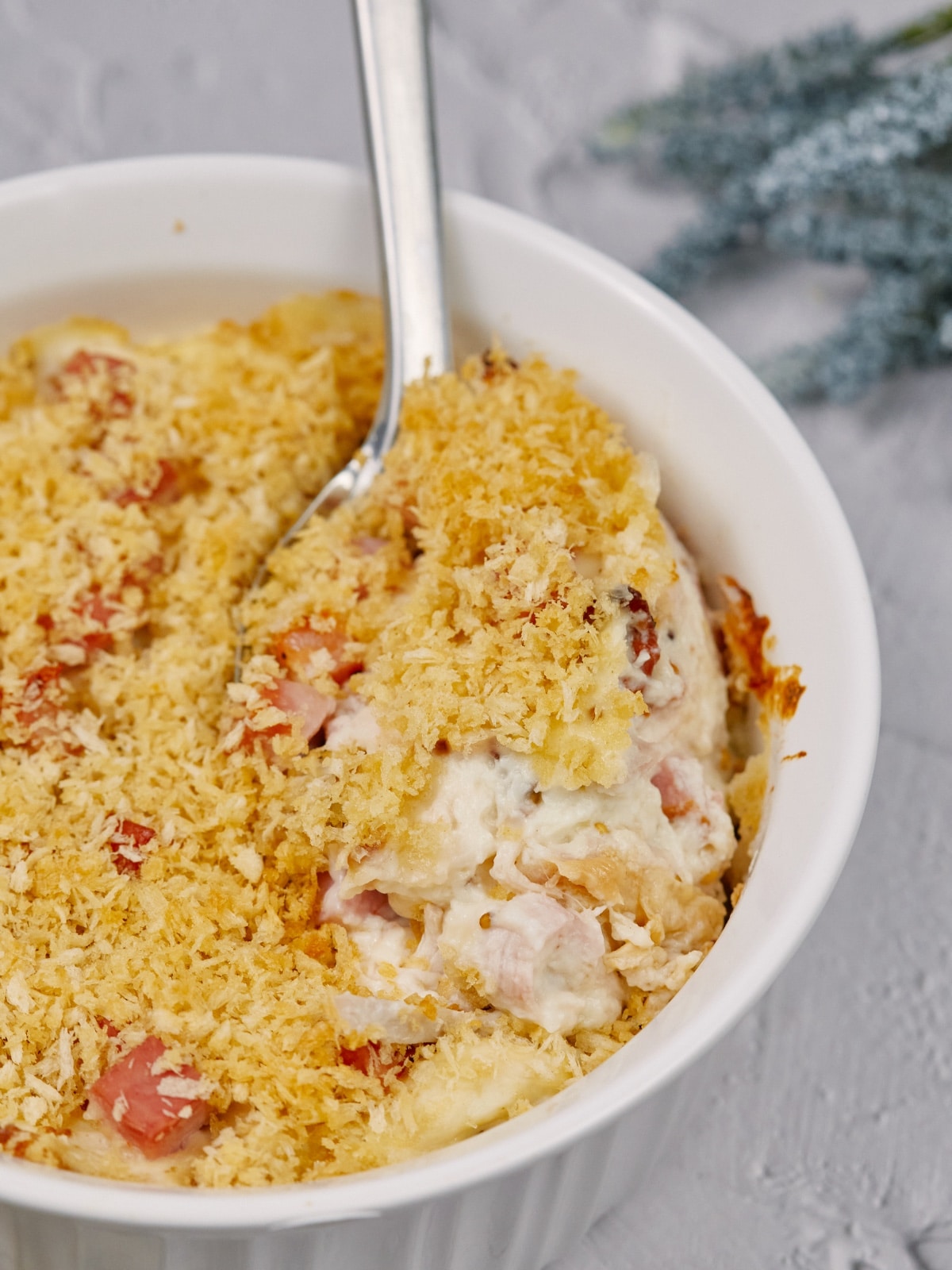 chicken cordon bleu casserole baked in a round dish and sitting on a white surface with a spoon in the middle