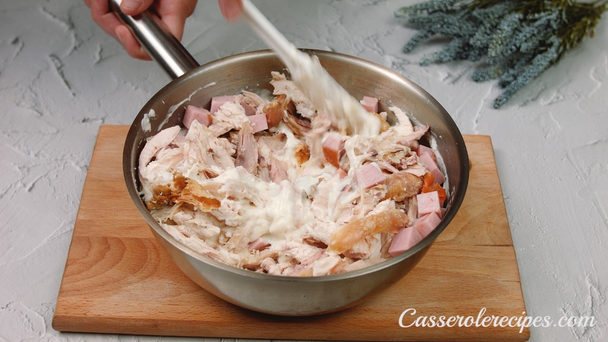 mixing the sauce, ham, and chicken together in the pot with tongs