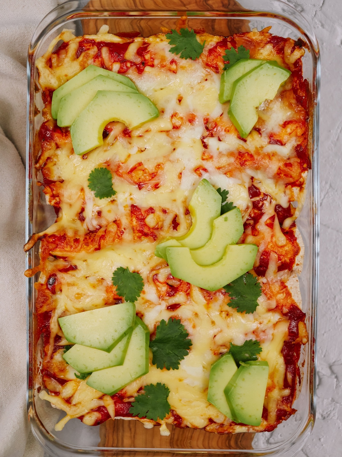 a overhead view of baked chicken enchiladas in a baking dish topped with cheese, cilantro, and avocado slices