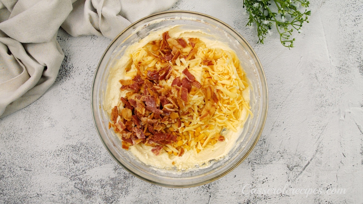 a yellow batter topped with cooked bacon pieces and cheese before mixing in