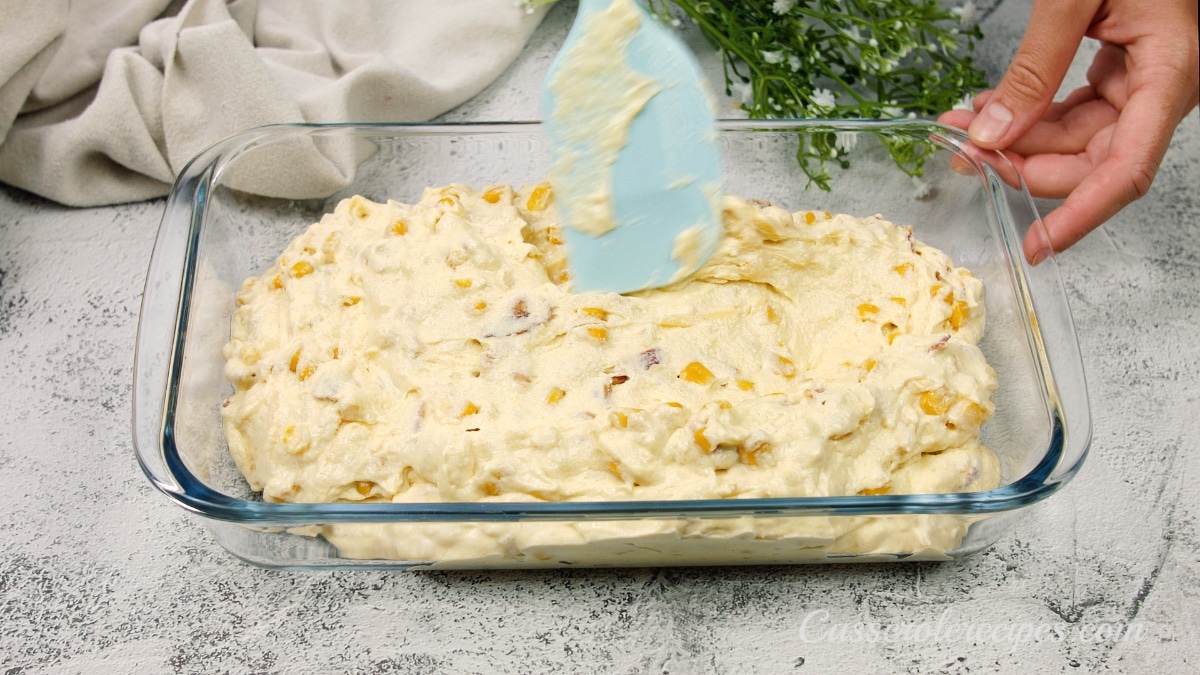 spreading the batter in a glass casserole dish with a blue plastic spatula