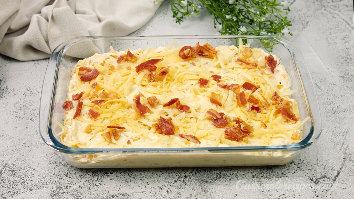 unbaked casserole in a glass dish topped with cheese and cooked bacon pieces