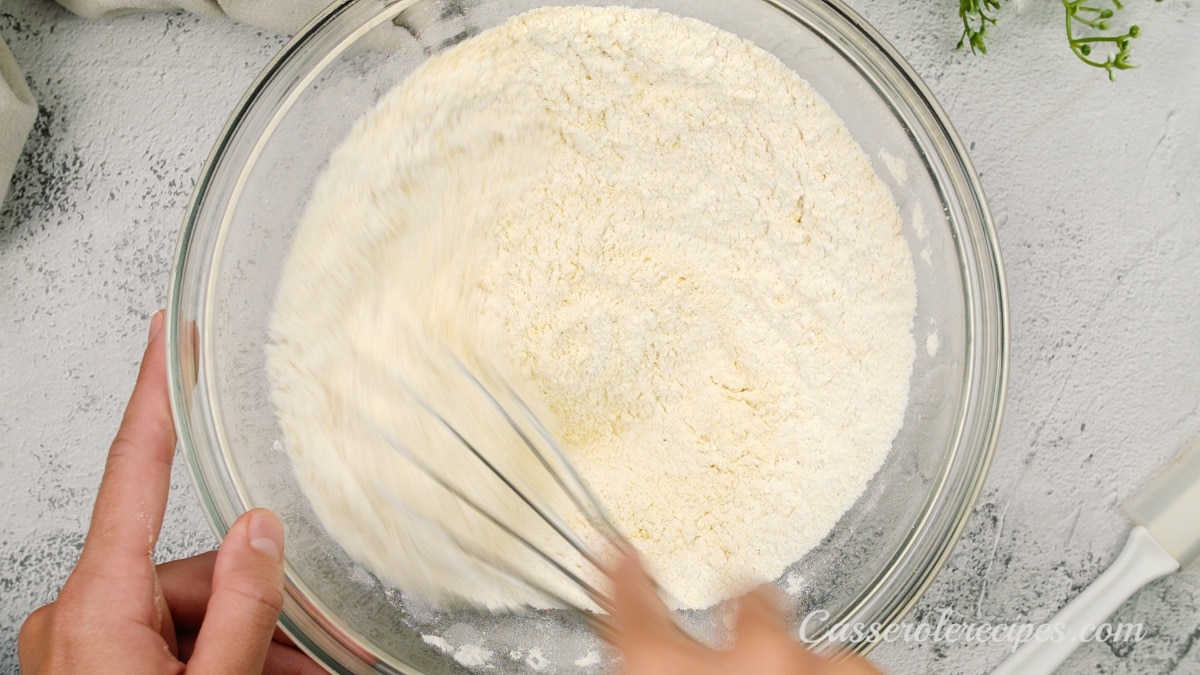 mixing flour and corn meal together in a bowl with a whisk