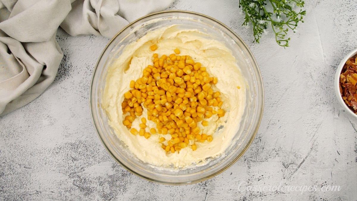 a thick yellow batter in a glass bowl topped with corn kernels