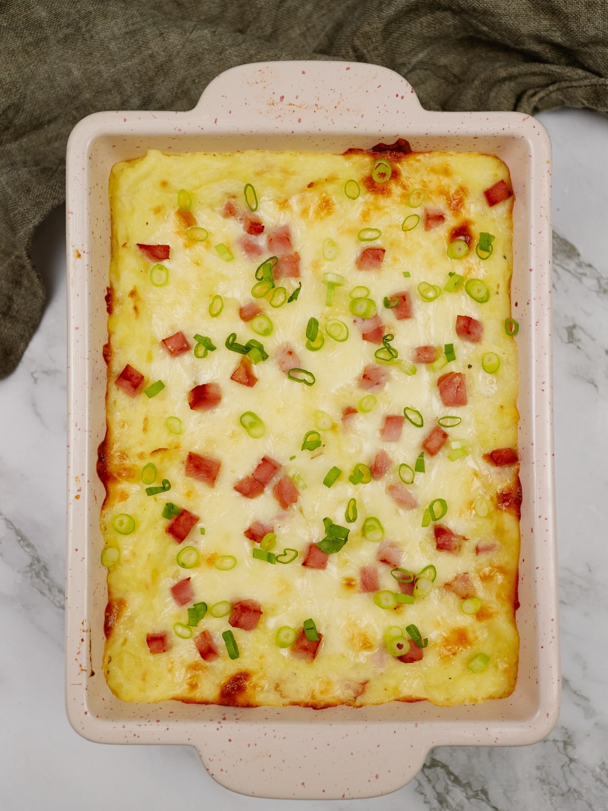 ham and potato casserole in a white dish on a marble counter