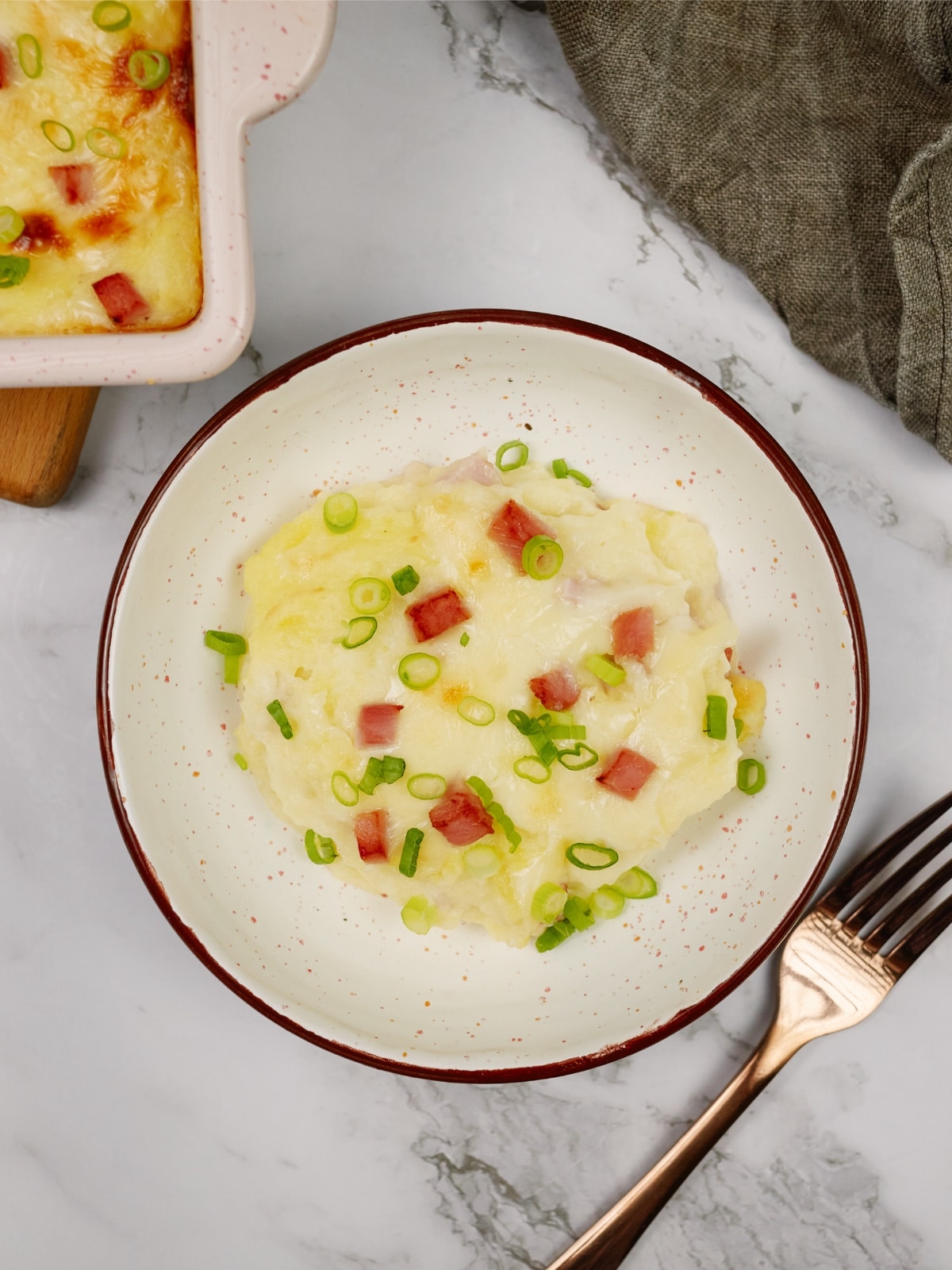 a bowl of ham and potato casserole with a fork sitting on the side