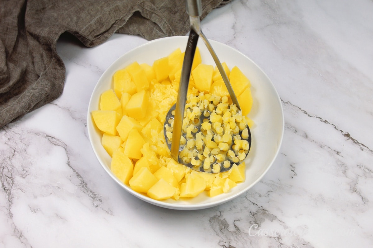 mashing potatoes in a white bowl with a potato masher