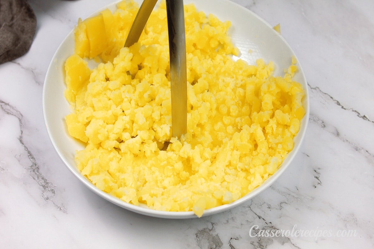 mashing potatoes in a white bowl with a potato masher