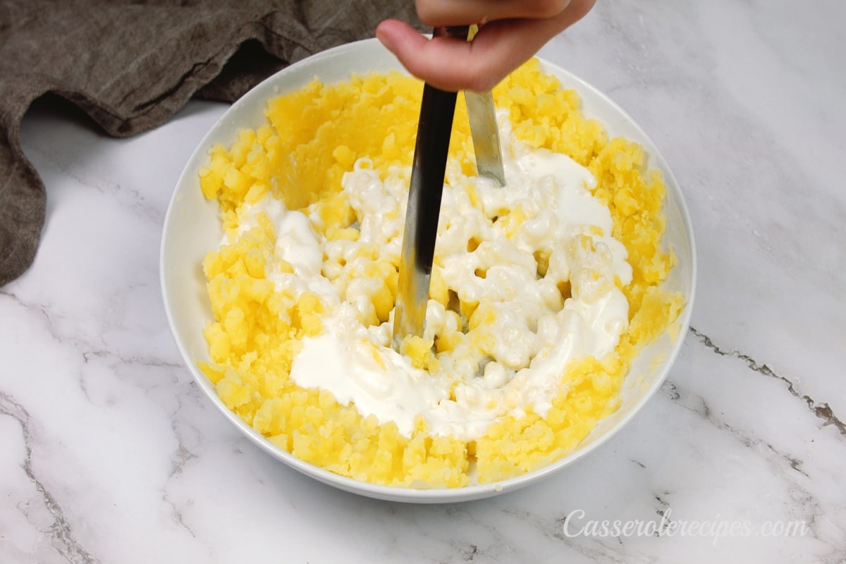 mixing in the sour cream and soup with a potato masher 