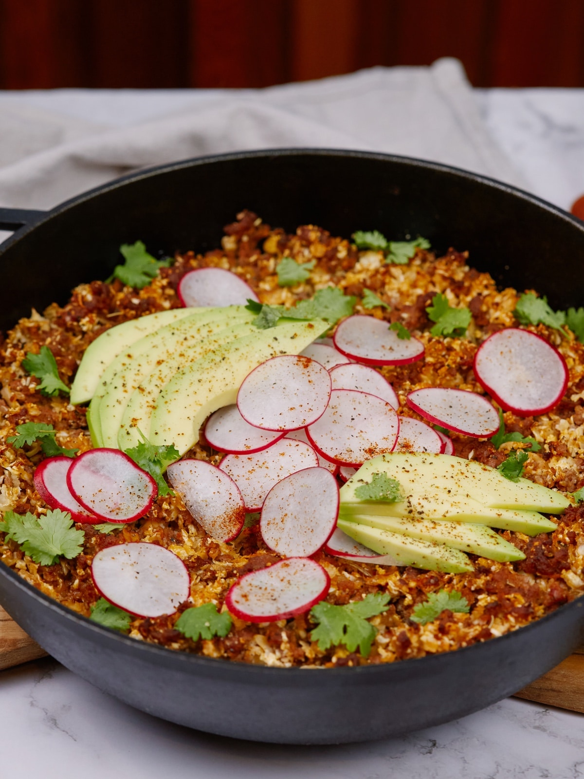 an overhead view of baked keto casserole topped with sliced radishes, avocados, and cilantro leaves