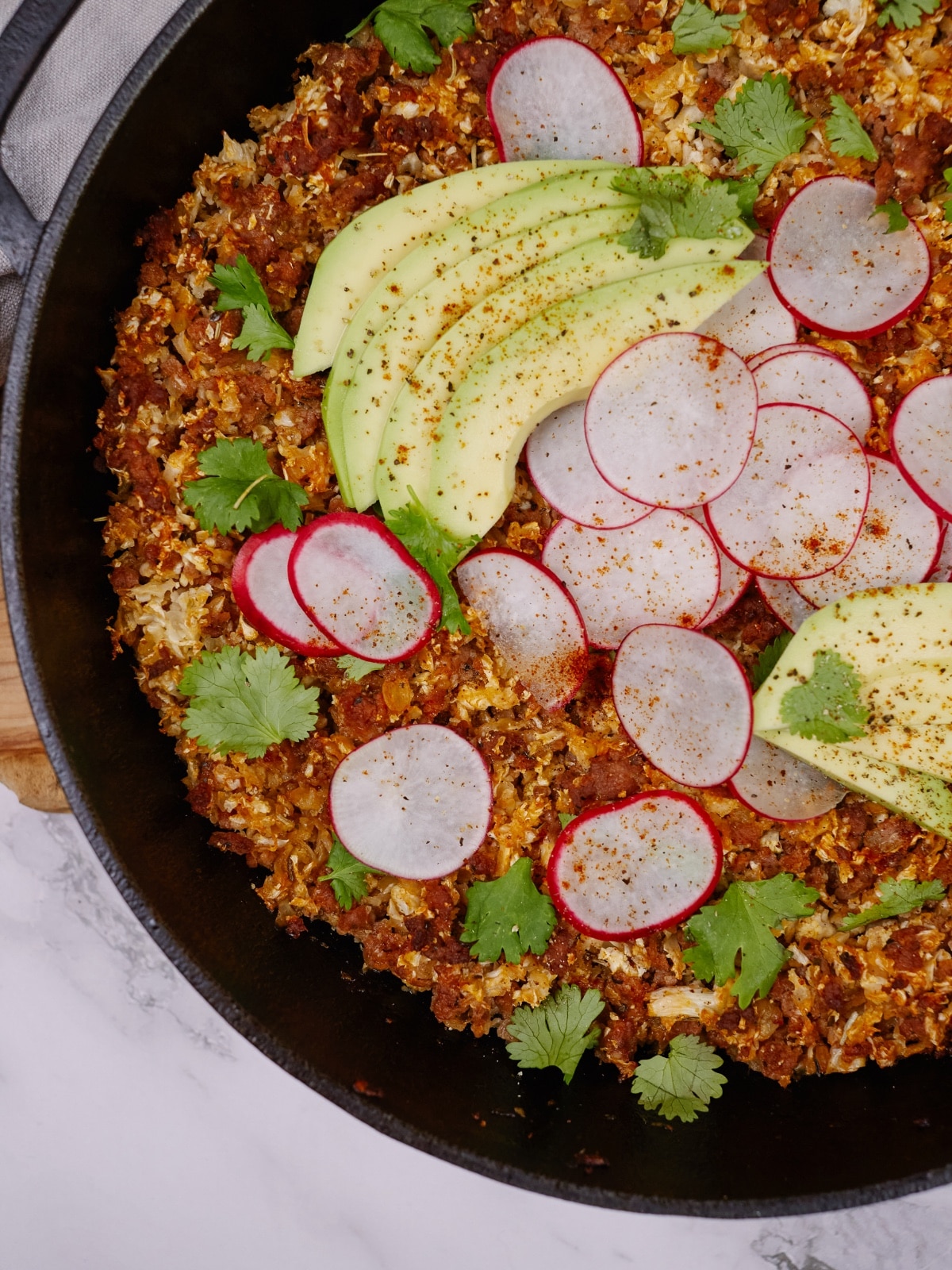an overhead view of baked keto casserole topped with sliced radishes, avocados, and cilantro leaves