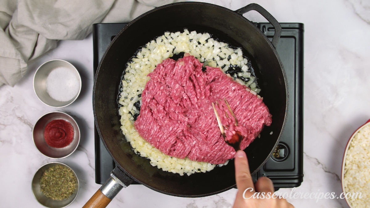 an overhead view of a pan with cooked onions and raw beef being mixed in on a stove top