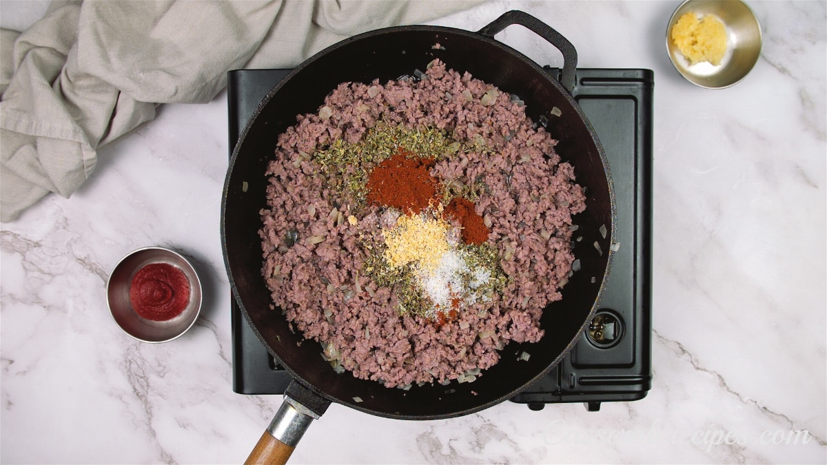 a pan of cooked ground beef in a pan with seasonings sitting on top waiting to be mixed in