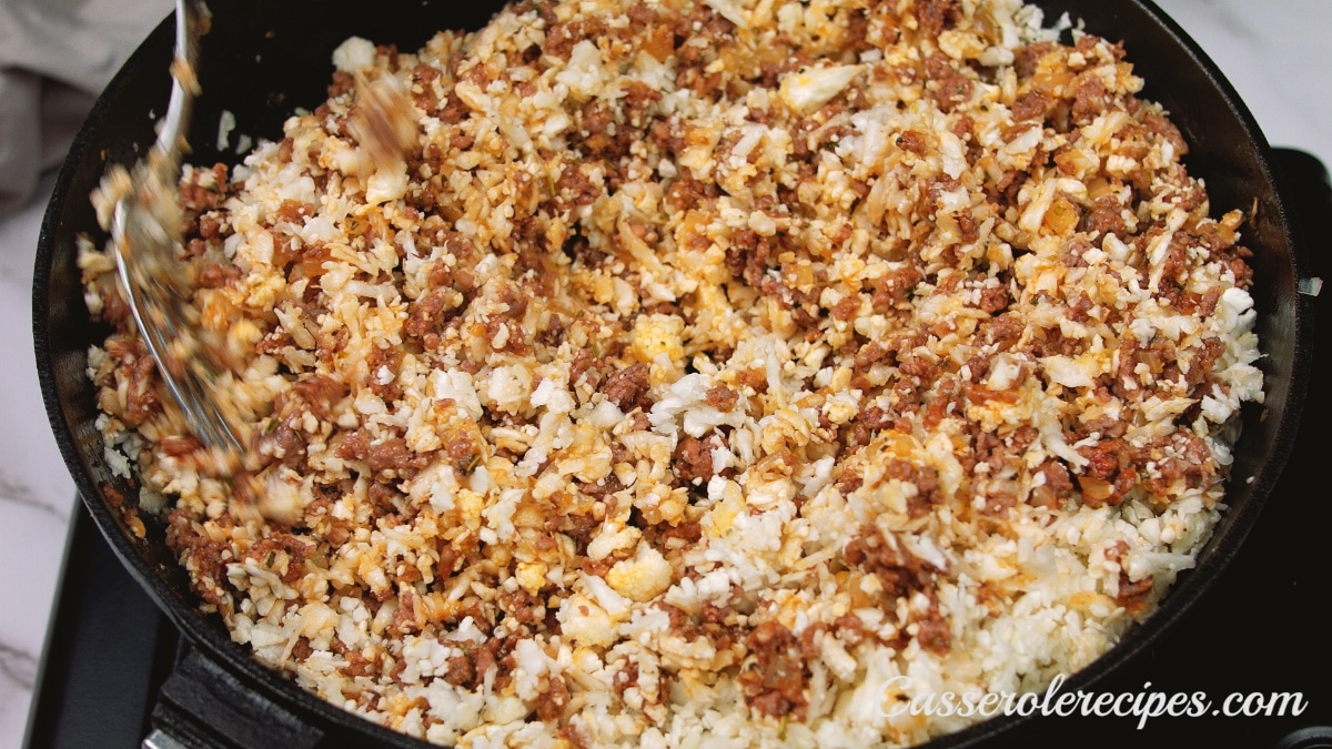 mixture of cauliflower rice, seasonings, onions, and beef in a cast iron skillet before baking