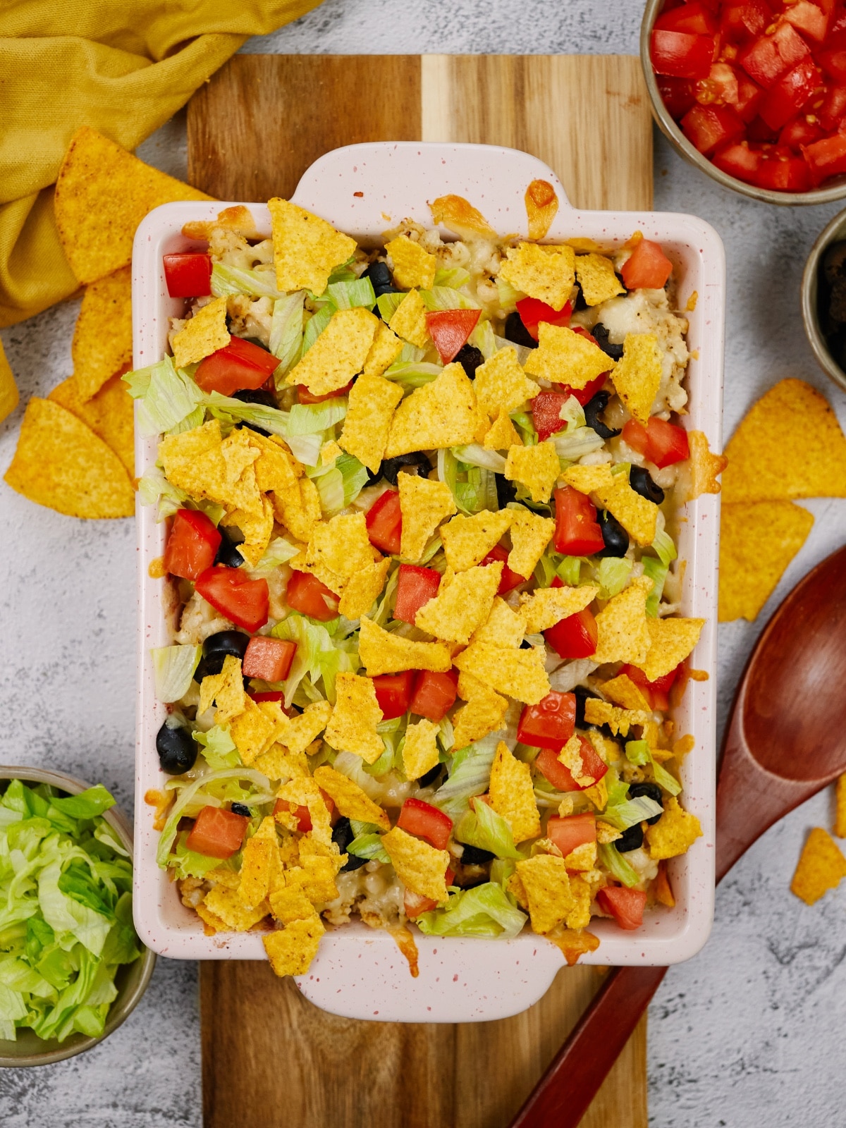 Mexican casserole in a white baking dish topped with tortilla chips, tomatoes, olives, and lettuce