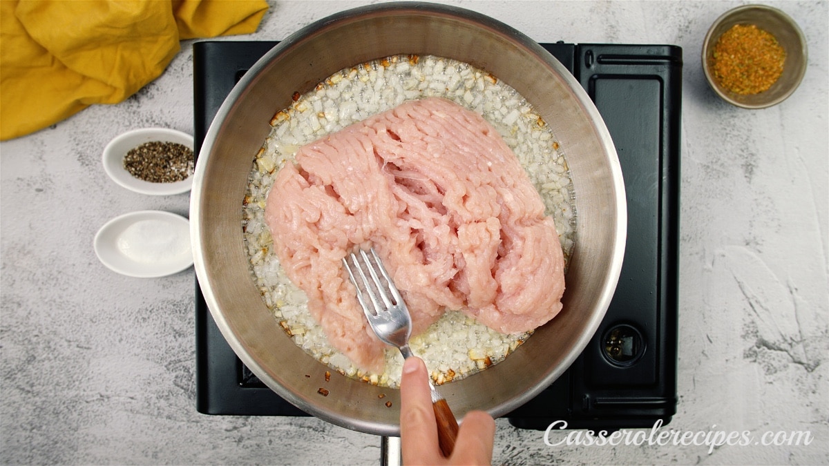 onions and raw ground chicken in a pan being mixed in with a fork