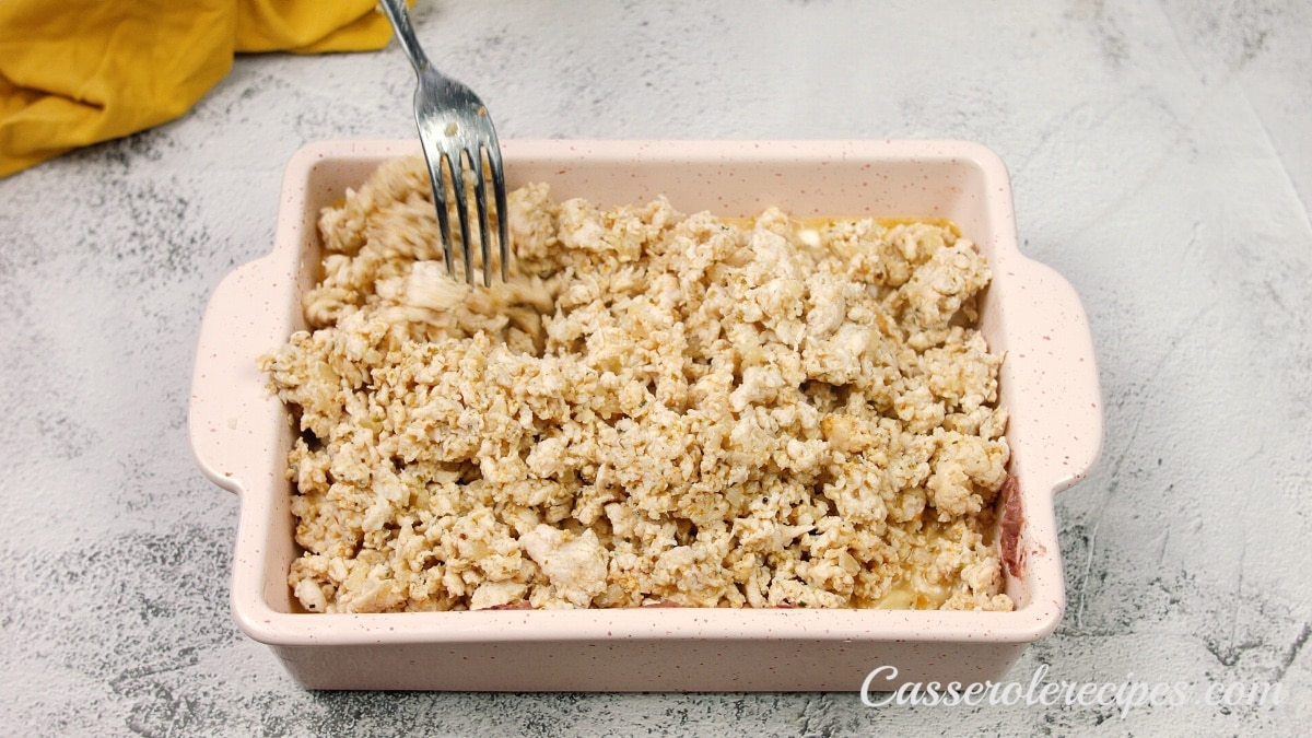 ground chicken mixture on top of sour cream and refried beans in a casserole dish