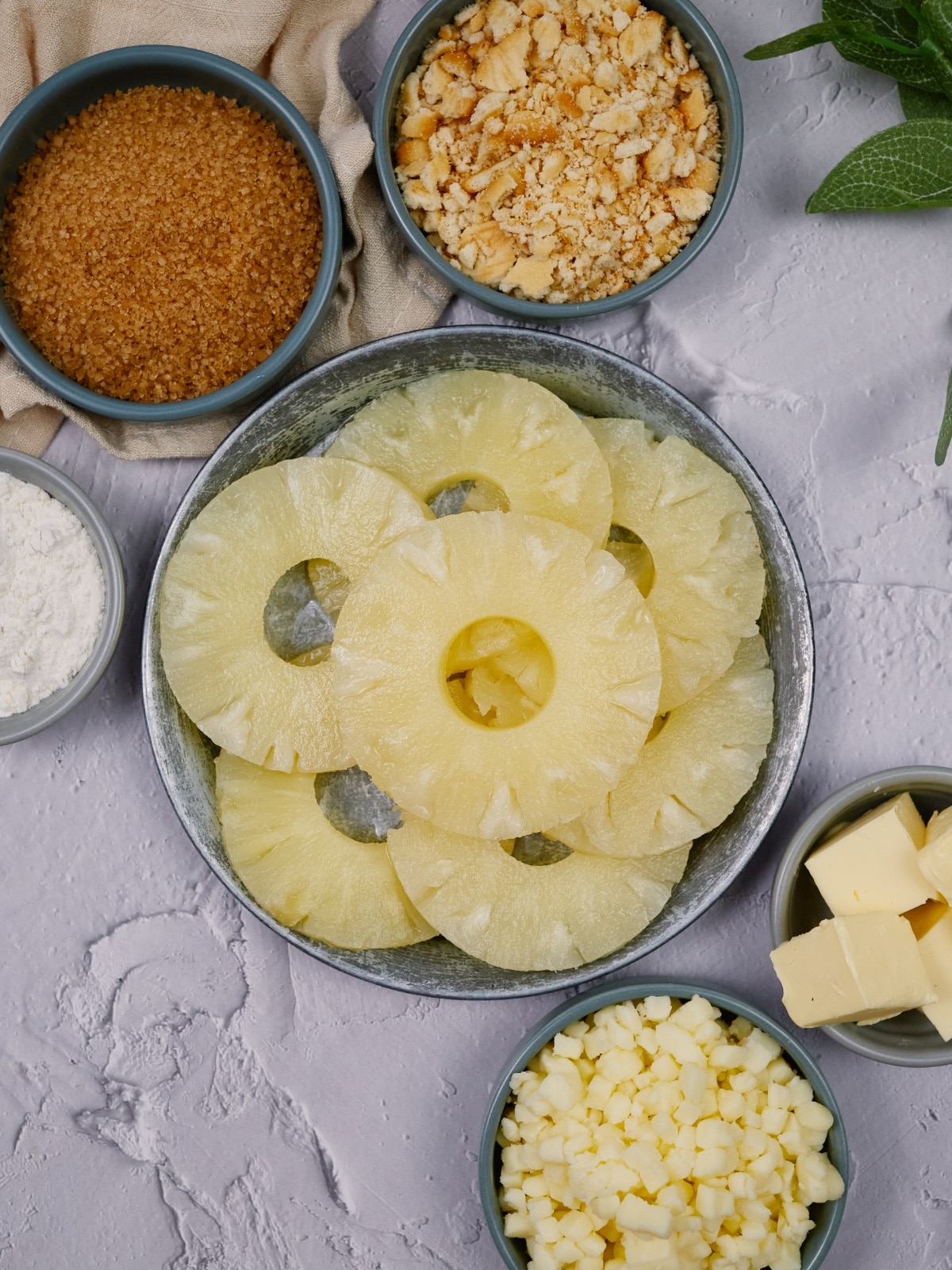 ingredients of pineapple casserole in small blue bowls on a white surface