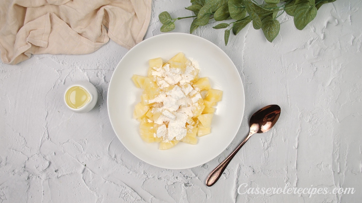 combining pineapples and flour in a white bowl