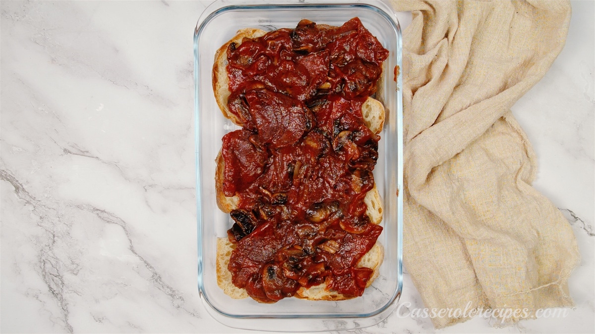browned mushrooms, onions, pepperoni, and red sauce in a glass baking dish sitting on a counter