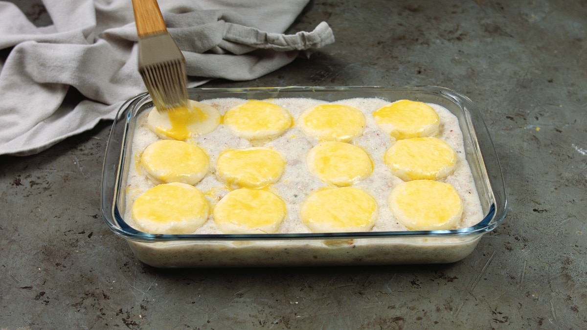 brushing egg wash over biscuits in baking dish