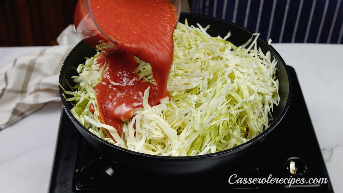 pouring tomato sauce over cabbage in skillet