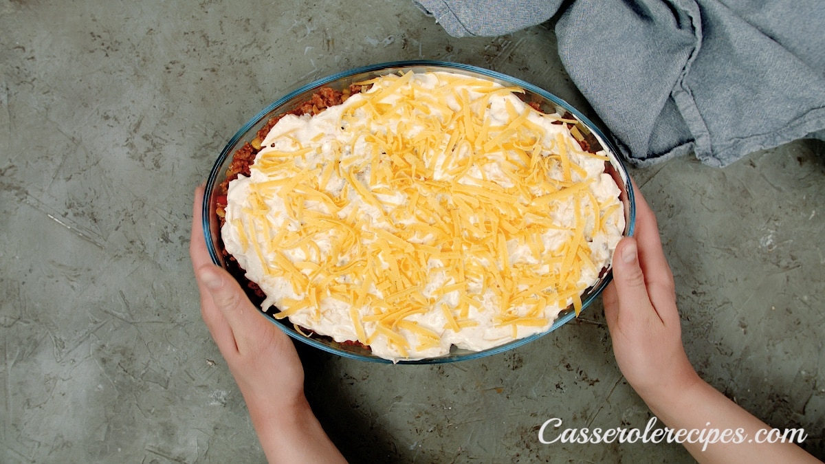 cheese sprinkled on top of the casserole held by two hands