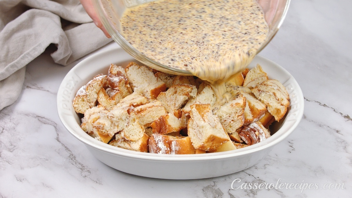 pouring egg mixture over cinnamon rolls in a baking dish