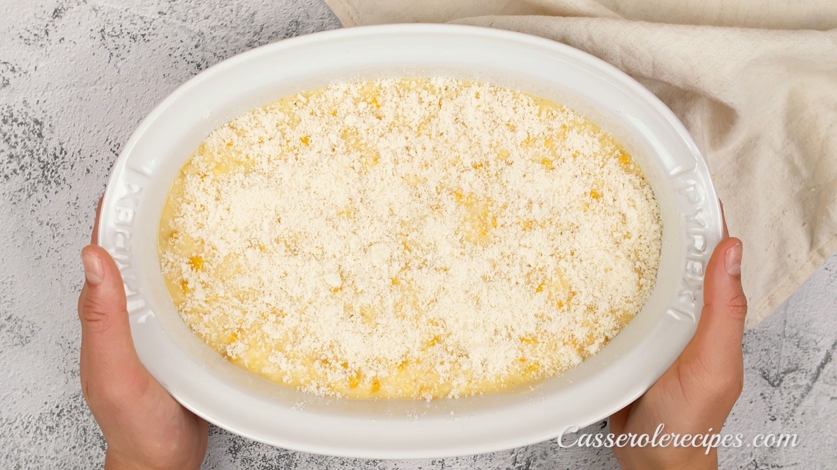 corn casserole topped with cheese being held by two hands