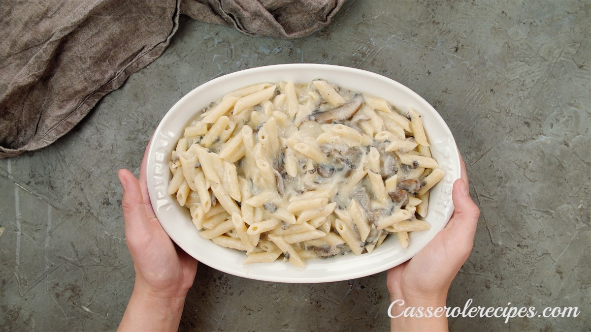creamy mushroom casserole held by two hands in a baking dish