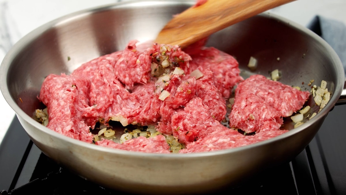 breaking up the ground beef with a wooden spoon in a pan