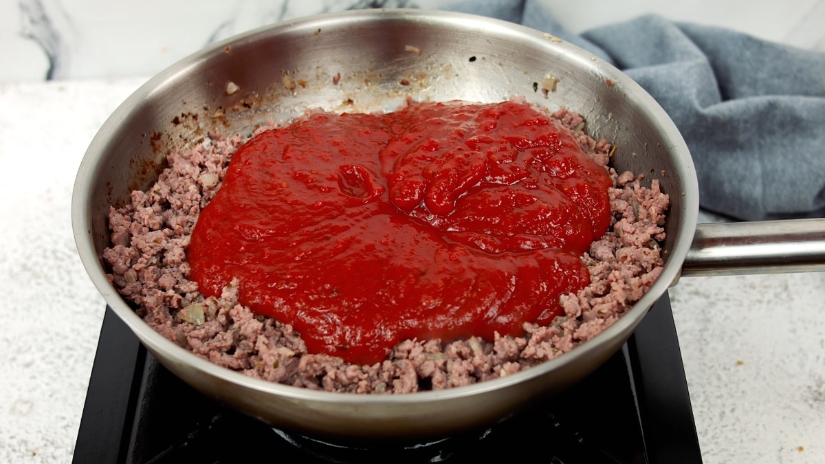 tomato sauce added to the ground beef in a pan