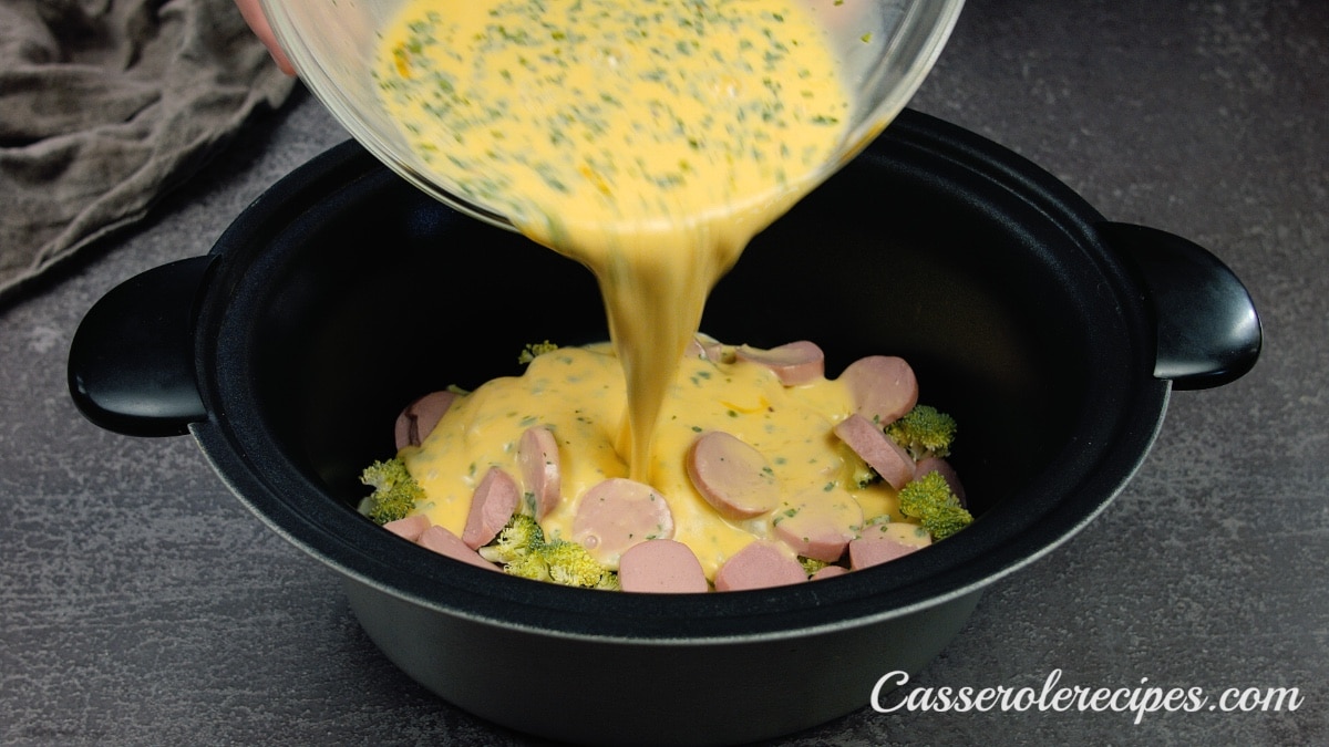 pouring egg mixture over broccoli in slow cooker