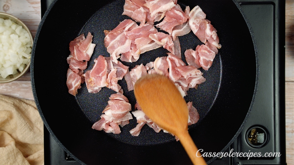 stirring bacon with a wooden spoon in a skillet