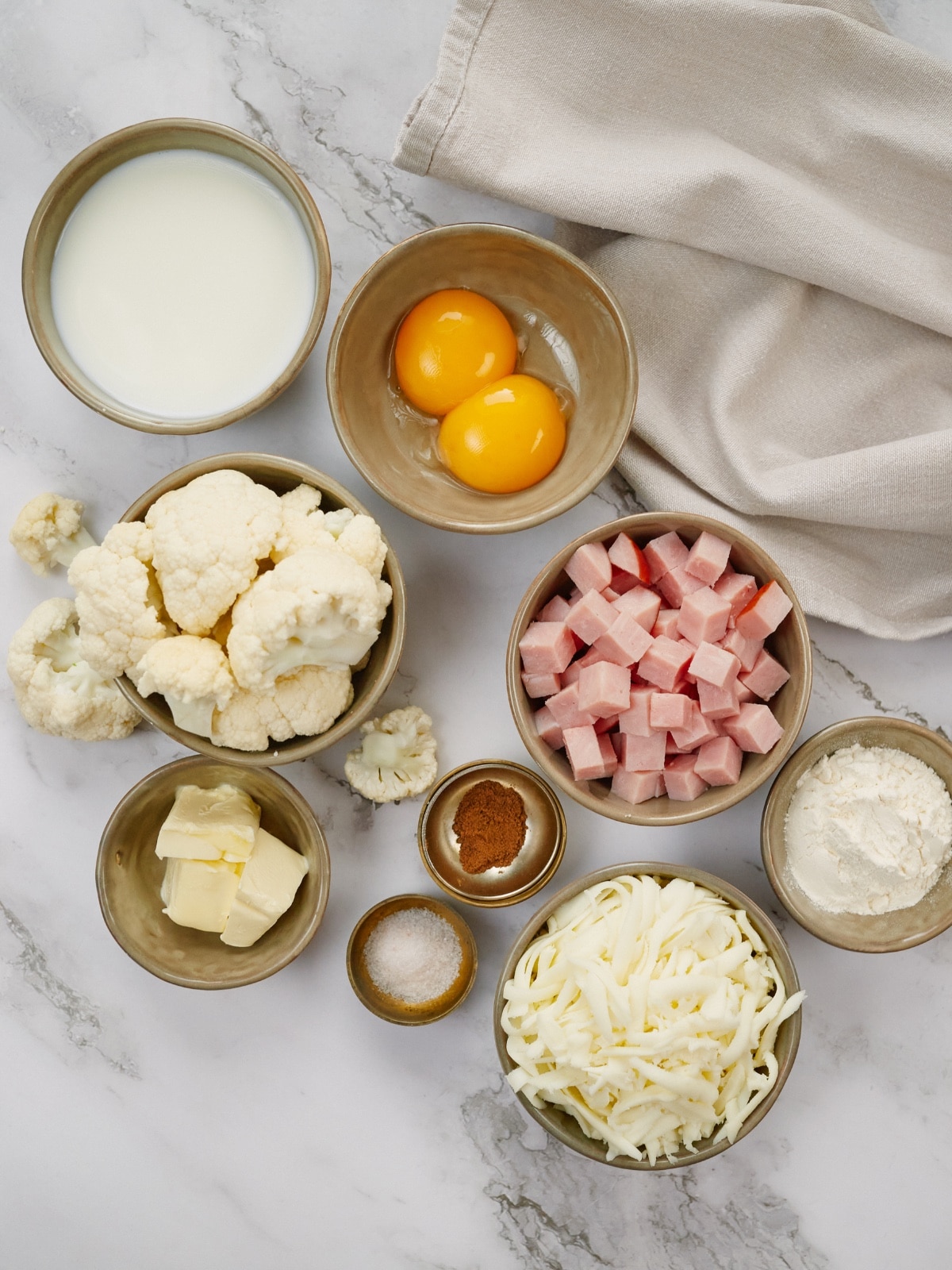 ingredients for ham and cauliflower casserole in small bowls on a light background