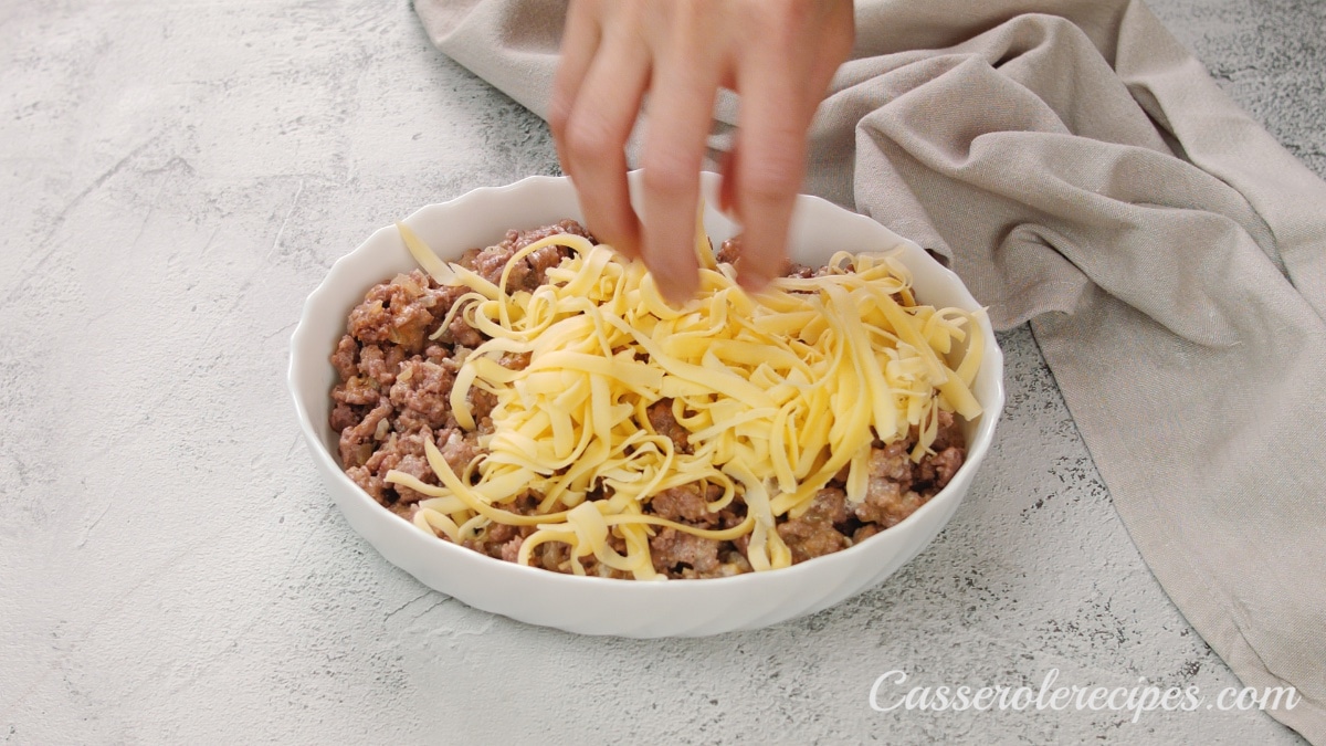 sprinkling cheese over beef in baking dish