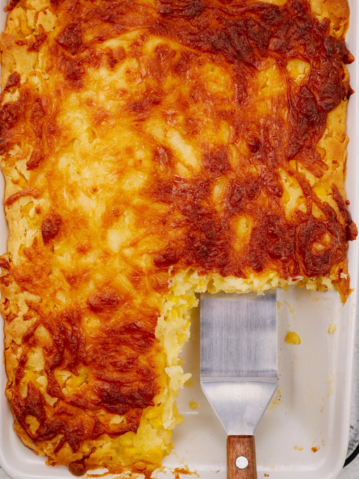 a metal spatula in the baking dish with corn casserole