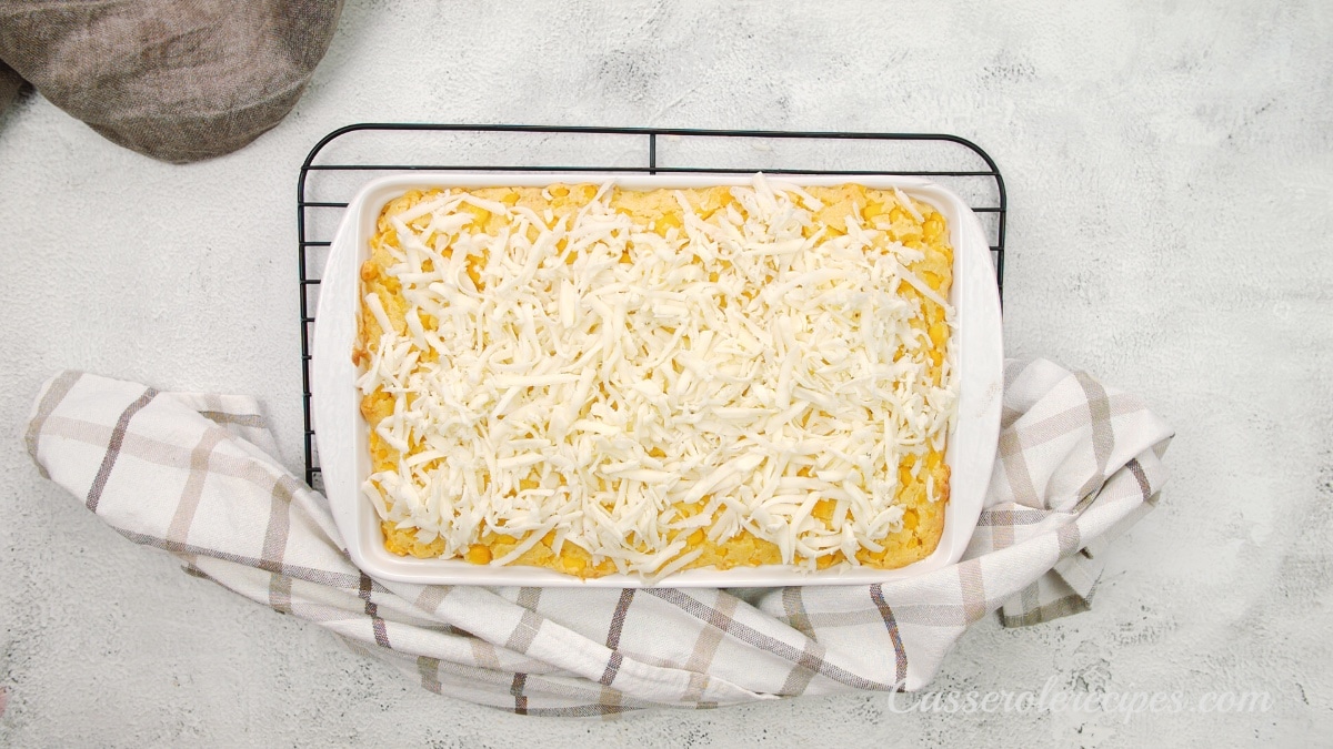 cheese topping corn casserole in a white baking dish