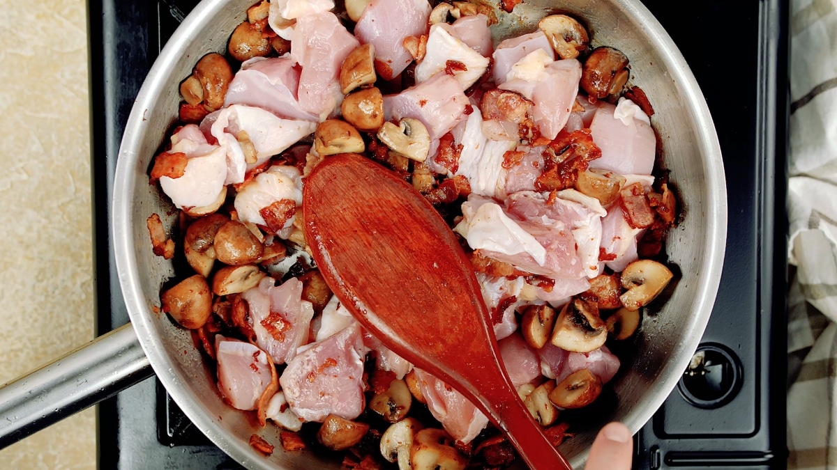 raw chicken chunks added to the pan and being stirred with a wooden spoon