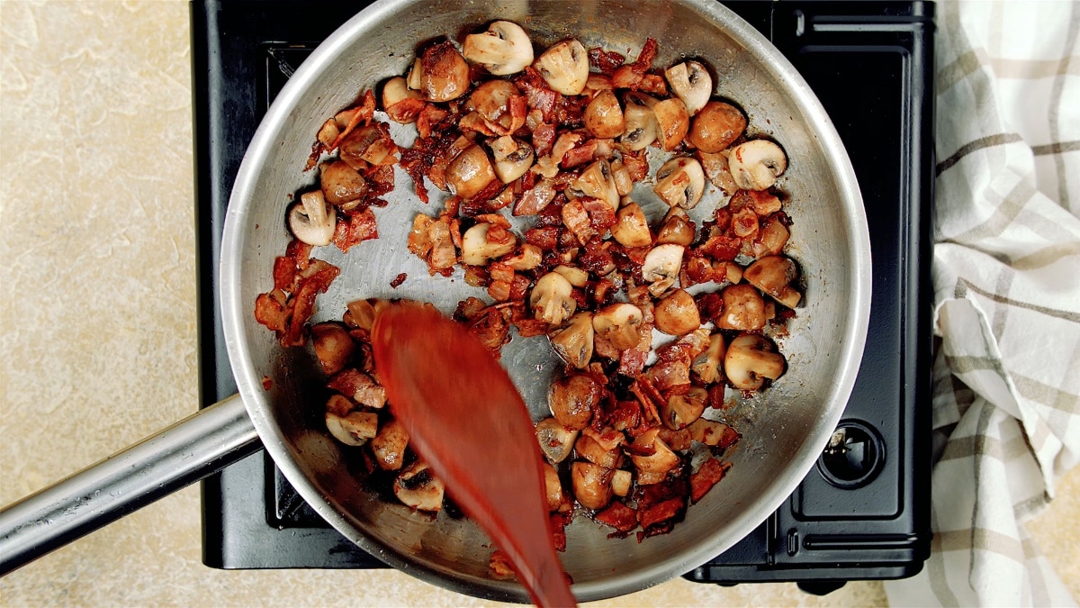 mushrooms and bacon being stirred with a wooden spoon