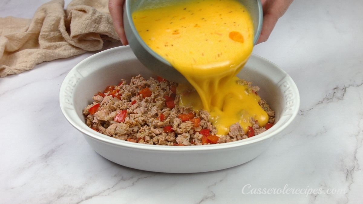 pouring egg mixture over the sausage in a baking dish