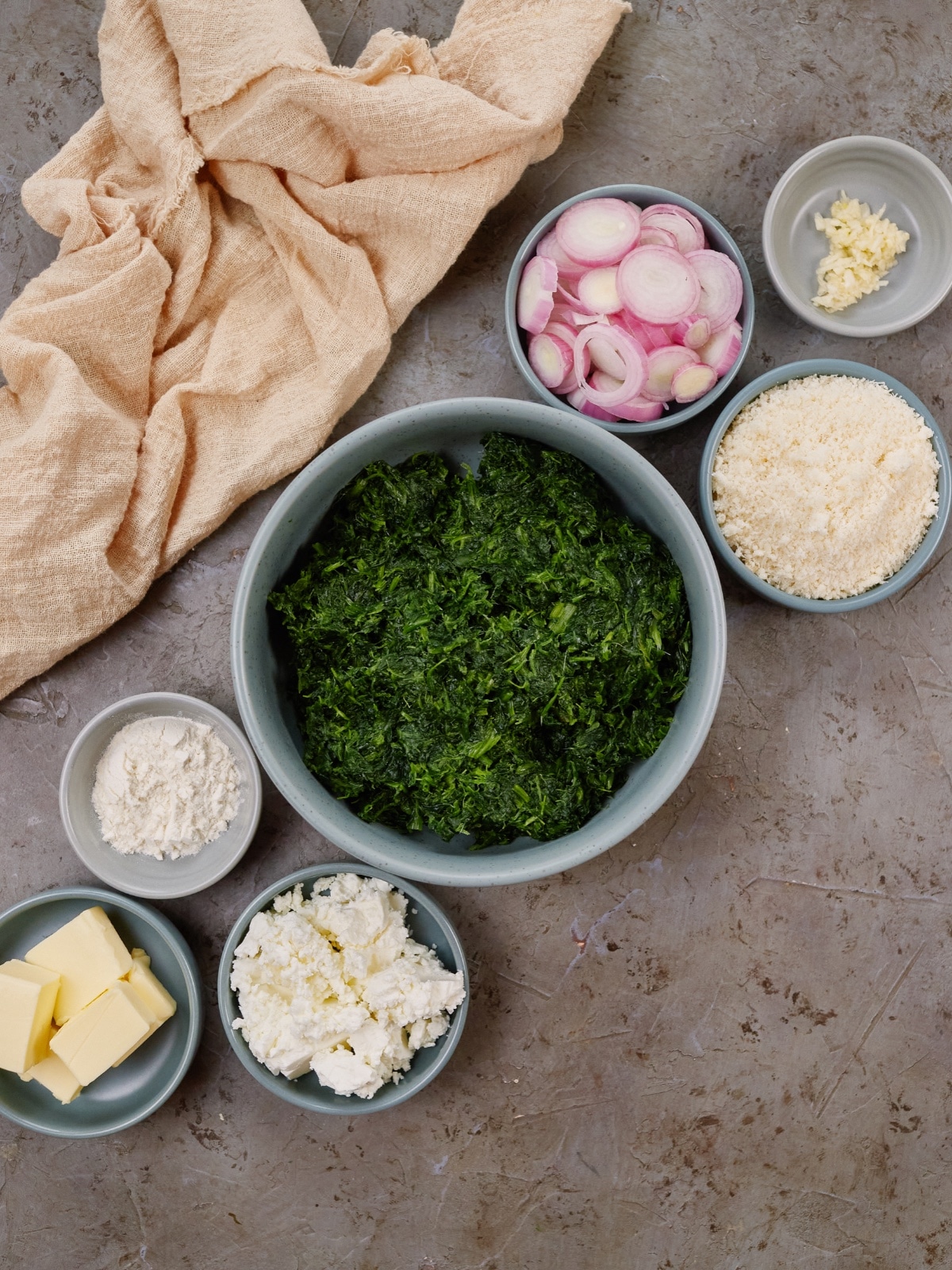 ingredients for spinach casserole in small bowls on a gray background